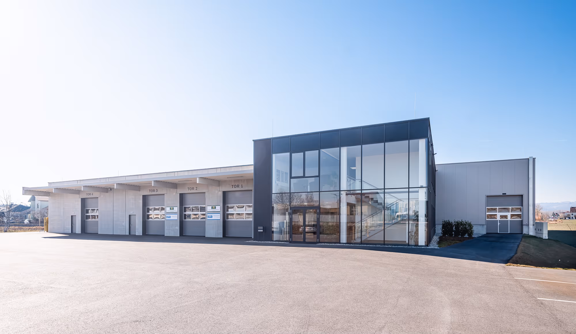 Modernes Industriegebäude der Spiro-Klima GmbH mit großem Glasfoyer und mehreren Laderampentüren unter strahlend blauem Himmel.